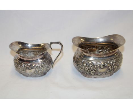 A silver plated oval milk jug with raised scroll decoration and matching sugar basin