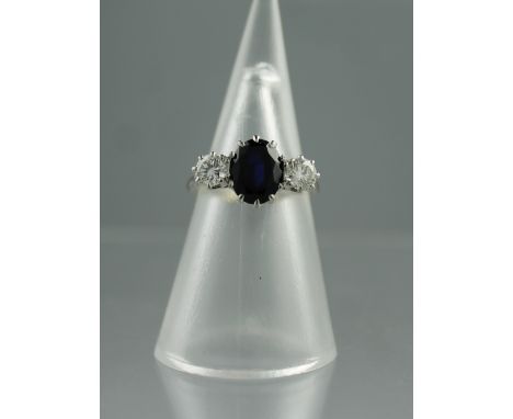 AN 18CT WHITE GOLD, SAPPHIRE AND DIAMOND RING.  The oval sapphire set to either side with a brilliant cut diamond.  Ring size