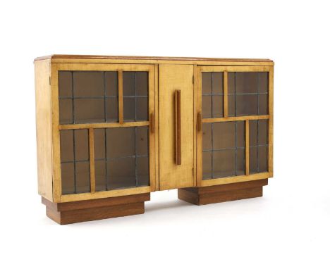 An Art Deco maple and oak low cabinet, fitted with two leaded glass cupboards, enclosing shelves, flanking a small central cu