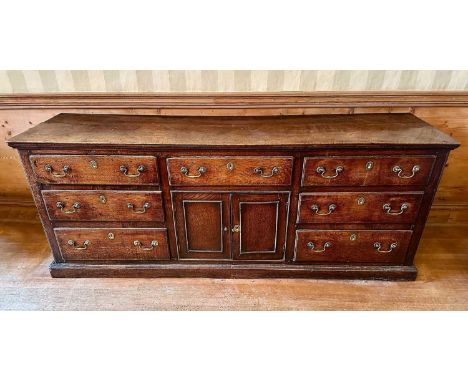 George III oak dresser base with an arrangement of seven drawers around central twin cupboards, with brass swan neck handles,