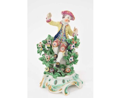 A Bow figure of a young boy singing, circa 1765, seated on a tree stump with bocage either side, polychrome painted, on a scr