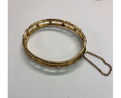 A yellow metal hinged bangle formed of a double row with beads between, concealed snap fitted with safety chain stamped 15ct,