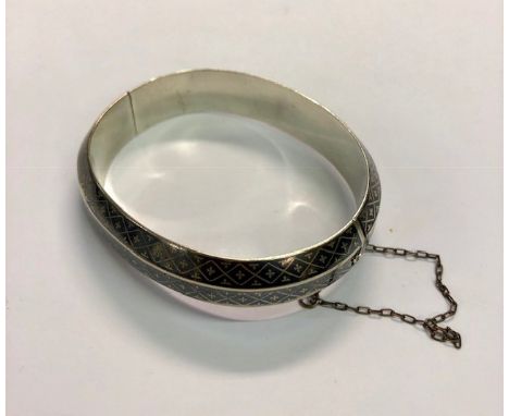 A white metal and niello decorated hinged and shaped bangle with safety chain attached