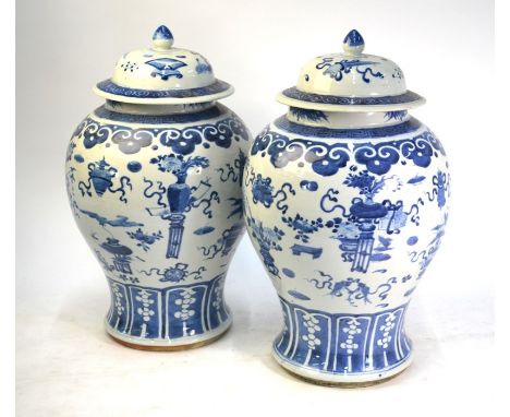 A pair of Chinese blue and white vases, each one with a domed cover and knop finial, decorated with sacred and scholar's obje