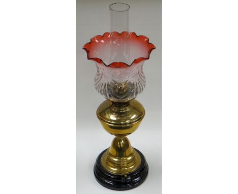 A VERITAS BRASS OIL LAMP ON A BLACK GLAZED POTTERY BASE and with cranberry tint floral shade, 47cms high