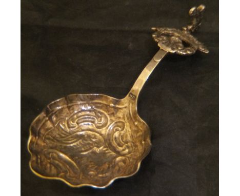 An 18th Century Continental white metal caddy spoon, the handle set with dancing cherubic figure set upon a crown to a shell-