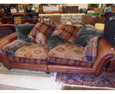 A three seat sofa in brown leather, the seats in cream and red upholstery with various cushions and large foot pouffe