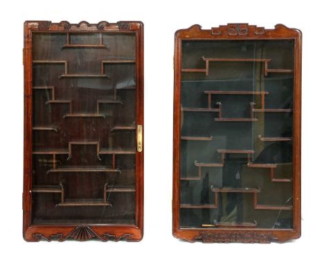 A near pair of Chinese carved hardwood hanging display cabinets, of slender form, having single glazed panel doors enclosing 