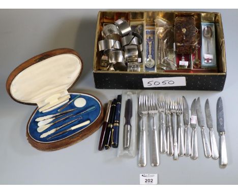 Box containing assorted souvenir spoons, silver plated napkins rings, loose plated cutlery, various pens, leather manicure se