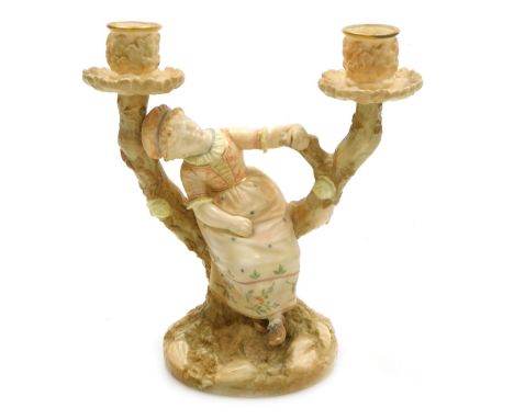 A Hadley's Royal Worcester blush porcelain figural candelabrum, modelled as a girl with a mob cap, seated on a bough of a tre