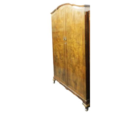 An early 20thC walnut double wardrobe, the shaped, domed pediment over two doors, enclosing a hanging rail and small shelf, r