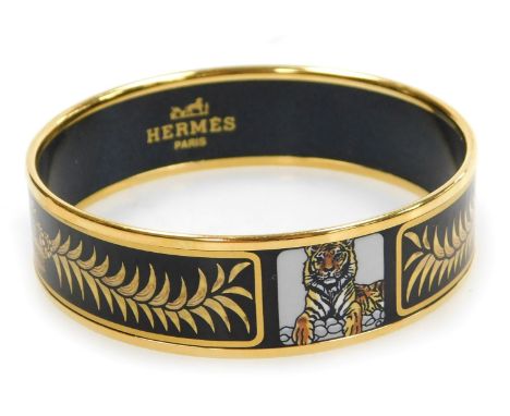 An Hermes gold plated and enamel bangle, decorated with tigers, crowns and wreaths, on a black ground, 6.5cm wide.
