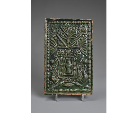 A GREEN-GLAZED POTTERY STOVE TILE, PROBABLY GERMAN AND 16TH CENTURY OR LATER. Moulded with vase issuing stylised flowers, wit