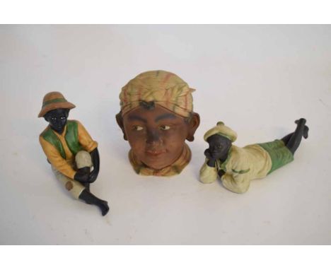 Two blackamoor porcelain figures of a seated gent and a further recumbent gent, together with a further blackamoor head of a 