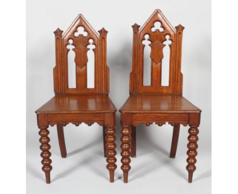 A pair of Victorian Gothic hall chairs, mid 19th century, with pierced arched high backs, pierced with trefoils and shield ca