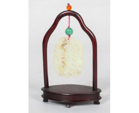 A Chinese carved pale celadon jade pendant and hardwood stand, of oval form, pierced and carved with inter-locking flower hea