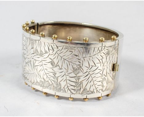 A 19th century aesthetic movement hinged silver bangle, engraved with fern leaves and set yellow metal ball motifs to the edg