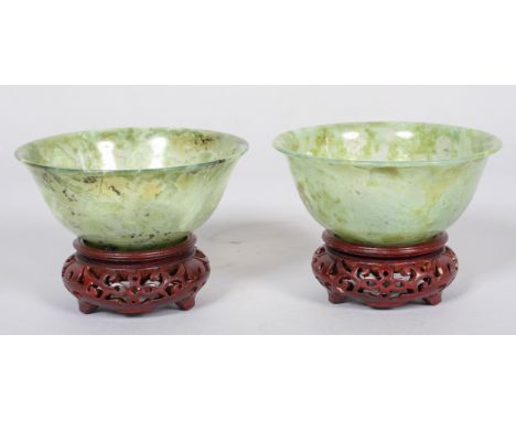 A pair of Chinese carved translucent green spinach jade bowls and hardwood stands, 20th century, each of overted form, of mot