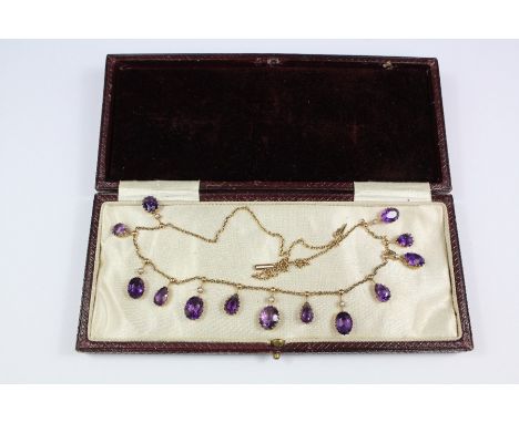 An Edwardian 9ct gold, amethyst and seed pearl necklace, the necklace set with seven graduated oval and six teardrop amethyst