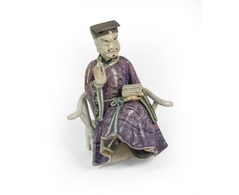 A Chinese Porcelain Figure of a Dignitary, Qianlong, sitting wearing purple robes, a scroll in his left hand, on a separate c