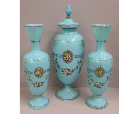 A pair of blue opaline glass vases and one taller lidded vase, enamel painted of swags of flowers and oval panels of flowers 