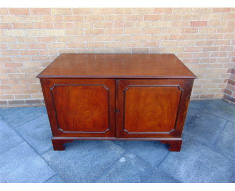 A MAHOGANY TWO DOOR CUPBOARD  with ornate brass carrying handles on bracket feet, the panelled doors opening to a sliding tra