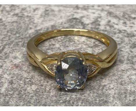 Ladies 9ct yellow gold blue stone and diamond ring, featuring a light blue stone set with a round brilliant cut diamond on ea