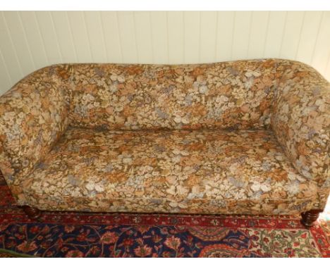 A Victorian club two-seater sofa, upholstered in a floral fabric, raised on turned supports and casters. 