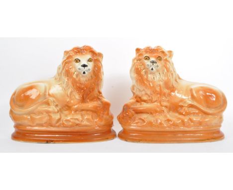 A matching pair of early 20th Century Staffordshire ceramic fire dogs in the form of lions having glass eyes with their cross