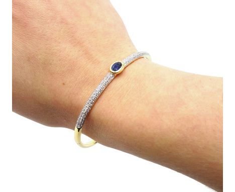 18ct gold hinged bangle, with a central rim set oval sapphire and pave set diamonds either side, stamped 750, sapphire 0.65 c