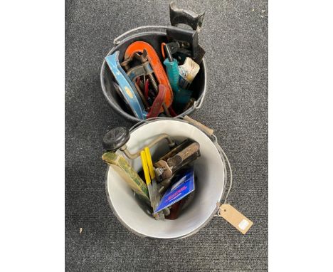 A plastic bucket and an enamel bucket containing assorted hand and power tools 