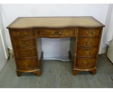 An early 20th century serpentine front kneehole desk with tooled leather top, nine drawers and brass handles on bracket feet