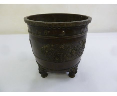 A 19th century Oriental bronze jardinière of cylindrical form decorated with flowers and butterflies on four mask feet