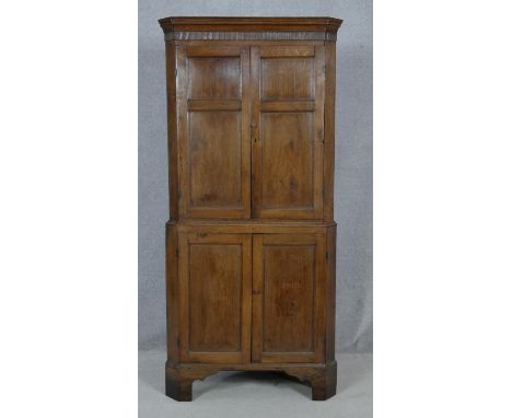 A Georgian oak two section corner cupboard with panel doors enclosing shelves on shaped bracket feet. H.179 W.82 D.49cm 