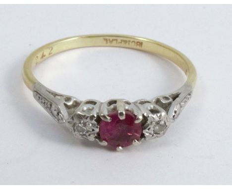 A ruby and diamond three stone ring, stamped '18ct Plat', the round cut stone between illusion set single cuts, finger size T