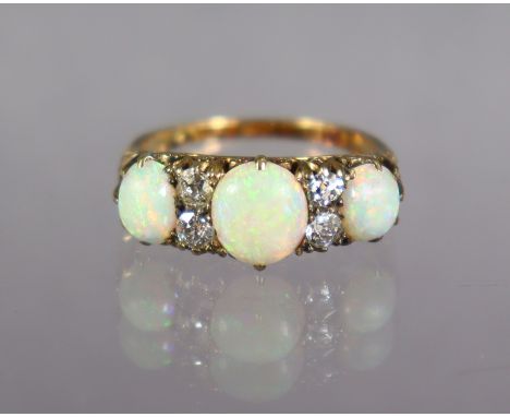 An opal &amp; diamond ring set three oval graduated opals, with pairs of small diamonds in between to a yellow metal shank ma