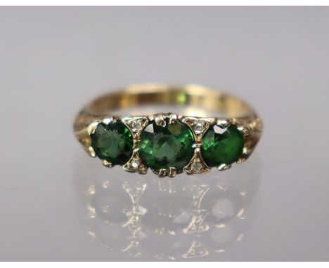 A 9ct gold ring set three graduated green stones with pairs of tiny diamonds in between; size: K; 2.7 gm.