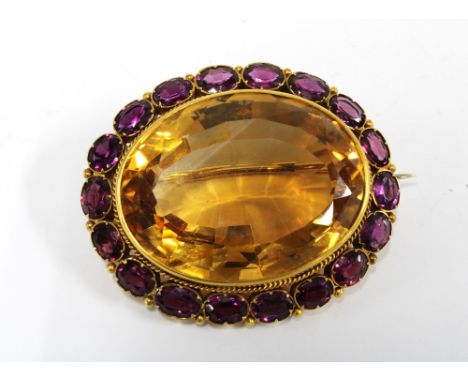 A citrine and rhodolite brooch, set in unmarked yellow metal, with a large oval citrine within a surround of rhodolite, 5cm