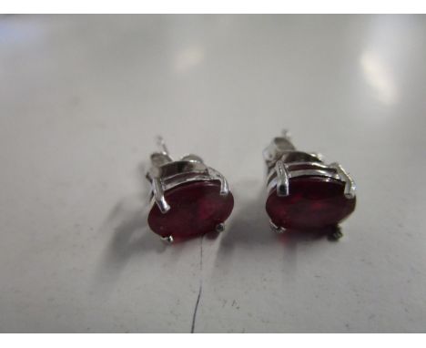 A pair of silver earrings, each set with a treated ruby 