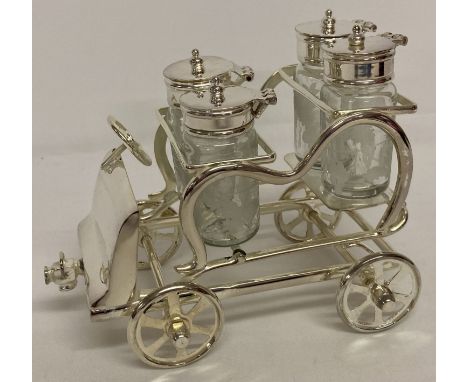 A novelty silver plated cruet stand in the shape of a vintage car.  Holding 4 etched glass condiment bottles with grape &amp;