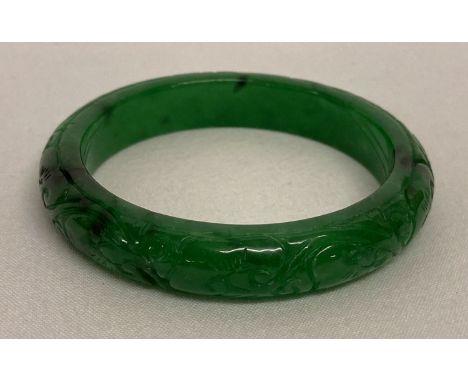 A Chinese green jade bangle with carved floral detail.   Approx. 7.5cm diameter.