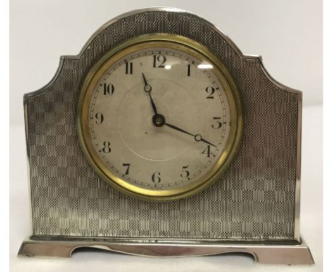 A small Art Deco silver table/bedside clock with chequered engine turned decoration.  Shaped base and top. Part of the wooden