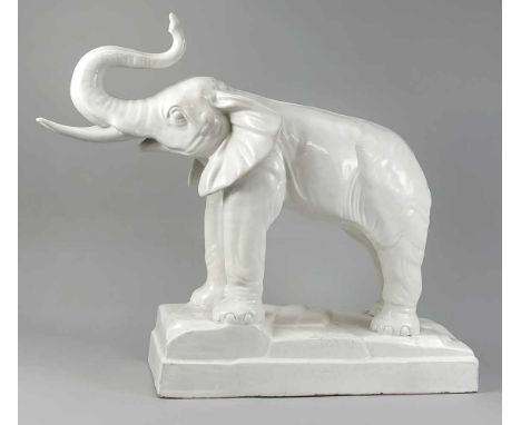 Stehender Elefant mit erhobenem Rüssel als Glücksbringer, 20. Jh., weiß, Terrainplinthe, Chips am Postament, Glasurfehler, 53