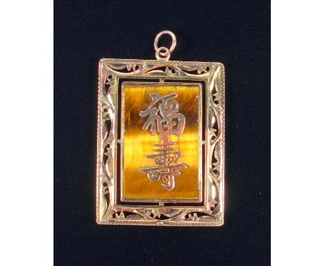 ORIENTAL YELLOW METAL RECTANGULAR PENDANT SET WITH A TIGER'S EYE PANEL WITH APPLIED SCRIPT, WITHIN A PIERCED SCROLL DECORATED