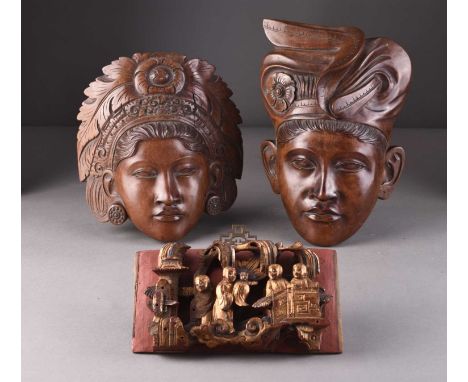 A pair of Balinese carved wood wall masksDepicting a male and female with elaborate headdresses, inscribed Klungkung Bali ver