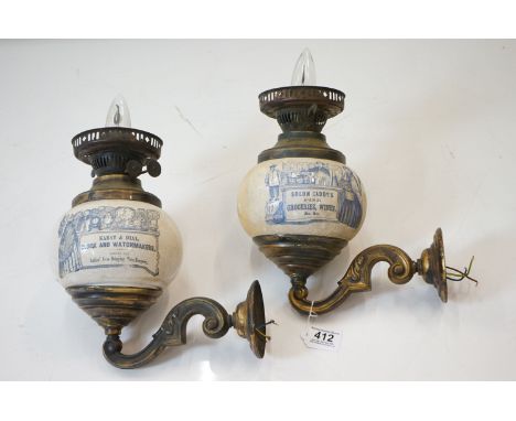 Pair of advertising brass wall oil lamps, the bulbous ceramic wells printed with advertisements for ' Karat &amp; Dial, Clock