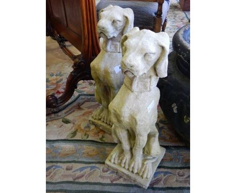 A pair of concrete garden ornaments in the form of seated dogs, on square bases