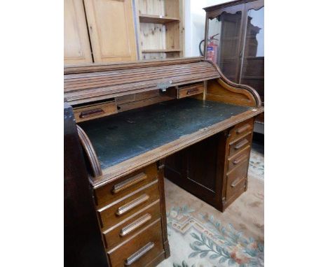 An oak roll top desk with tambour front enclosing pigeon holes and drawers, green leather writing surface and drawers to each
