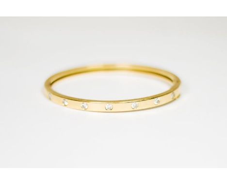 A gold stiff hinged bangle set with seven diamonds - 6 1/2cm dia.