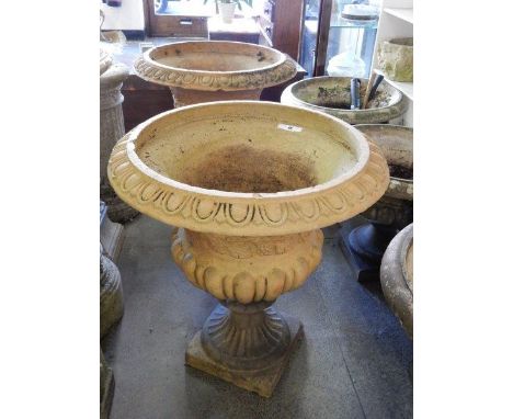 A pair of large terracotta garden urns with hop and vine leaf decoration, on fluted bases